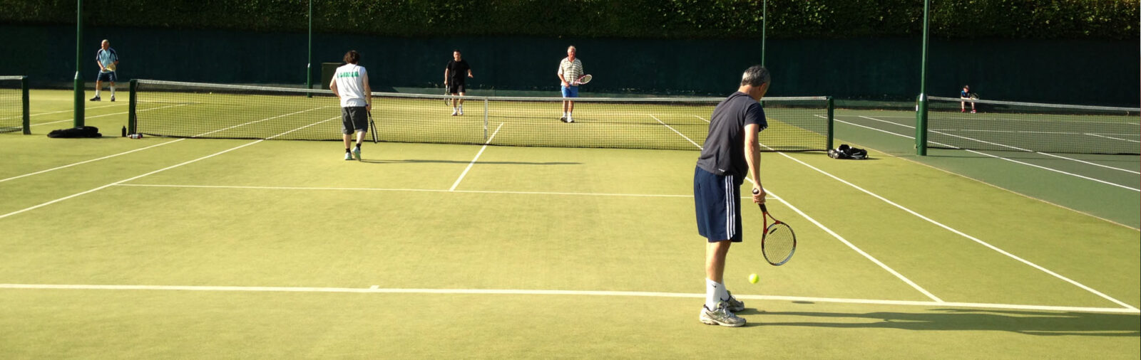 The nearest doubles partner serving on an astroturf tennis court at Bath Tennis