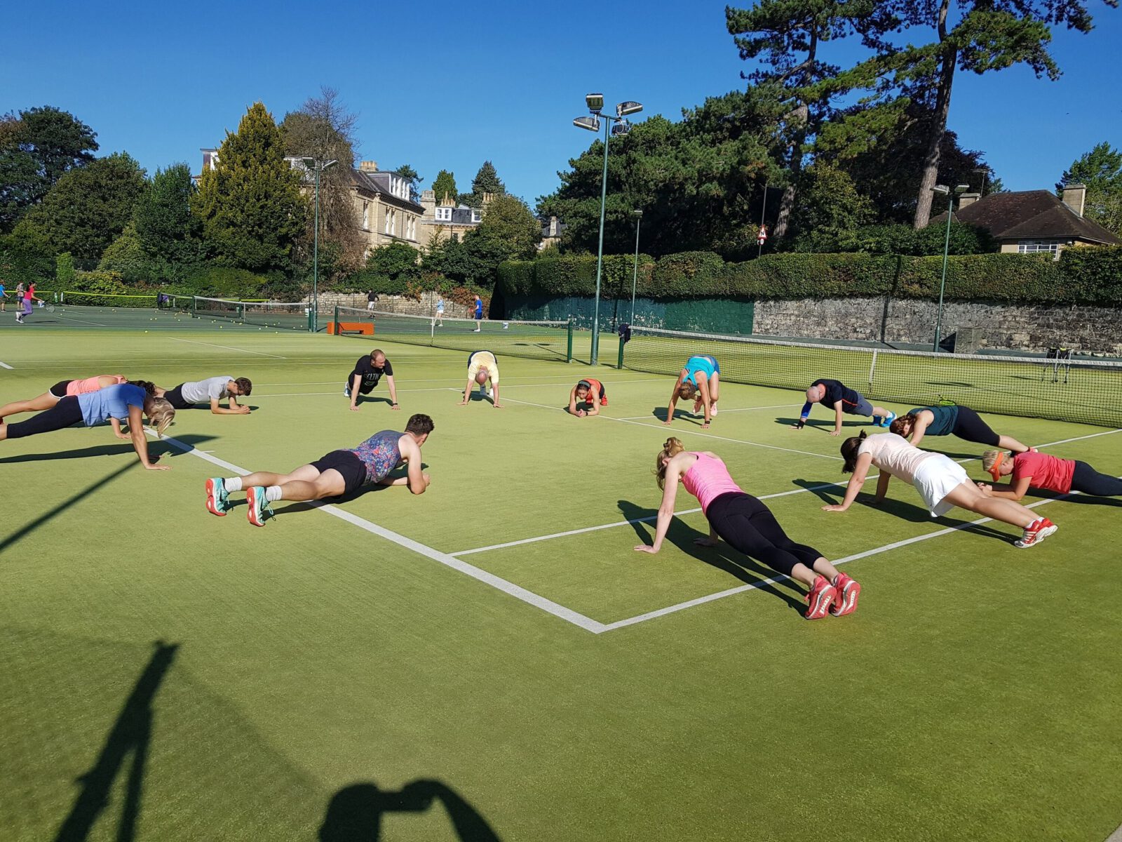 Multiple tennis players planking on the newly resurfaced astroturf tennis courts in a cardio tennis group session at Bath Tennis